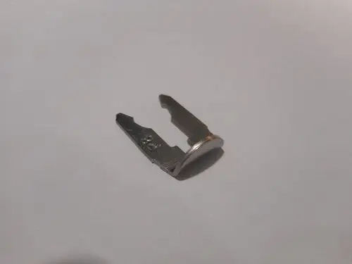 Remeha Clip, metallisch, mit einem flachen Ende und zwei Zinken, gekrümmt und asymmetrisch, auf weißem Hintergrund positioniert.